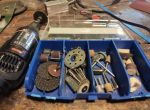 Ein Dremel-Multitool liegt auf einer Werkbank neben einer geöffneten Box mit verschiedenen Schleif-, Fräs- und Polieraufsätzen.