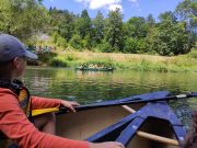Kind sitzt in einem Kanu auf einem Fluss, im Hintergrund paddelt eine weitere Gruppe.