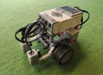 Ein LEGO-Roboter mit Sensoren und Kabeln steht auf einem grünen Teppichboden.