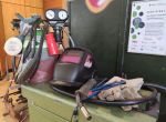 Schweißausrüstung mit Gasflasche, Schweißhelm, Handschuhen und Schläuchen steht auf einem Werkstatttisch.