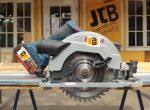 Eine Handkreissäge steht auf einem Arbeitstisch vor einem Gebäude mit der Aufschrift „JTB“.