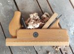 Ein Holzhobel mit Spänen liegt auf einer Holzoberfläche.